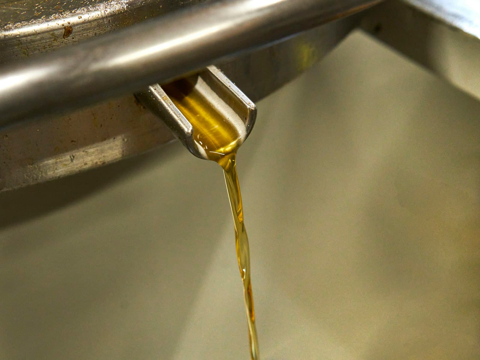 Olio appena estratto che scende da un beccuccio d'acciaio